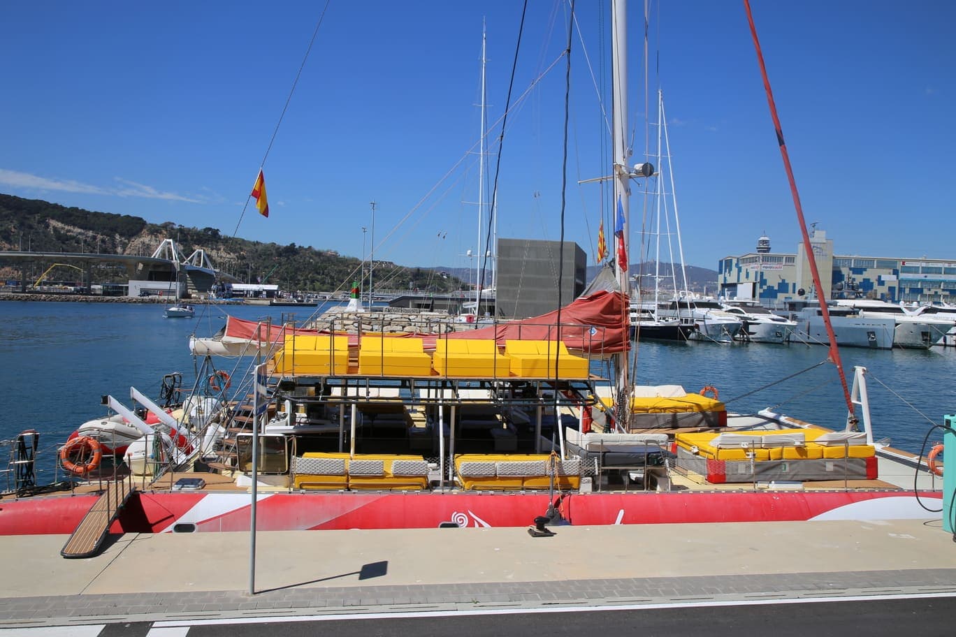 Catamarán rojo con cojines amarillos amarrado en el puerto con vistas al skyline