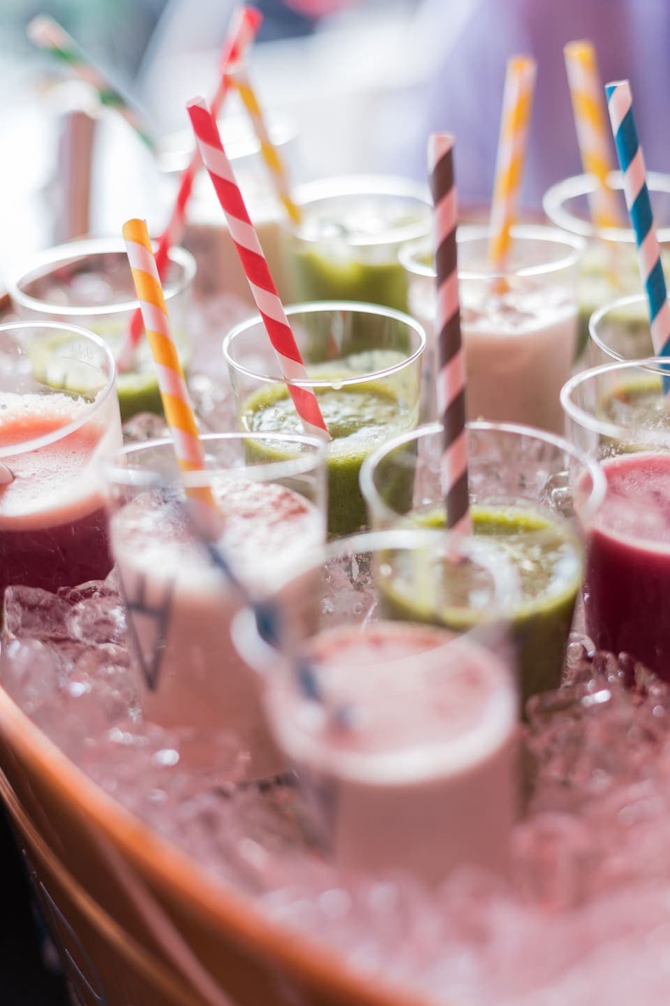 Bandeja de zumos y batidos de colores servidos en vasos con pajitas sobre hielo