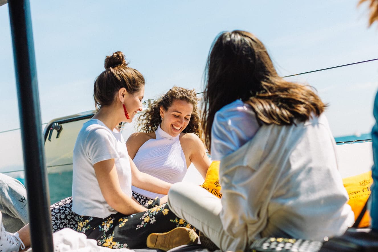 Grupo de amigas riendo juntas en la cubierta de un barco frente al mar