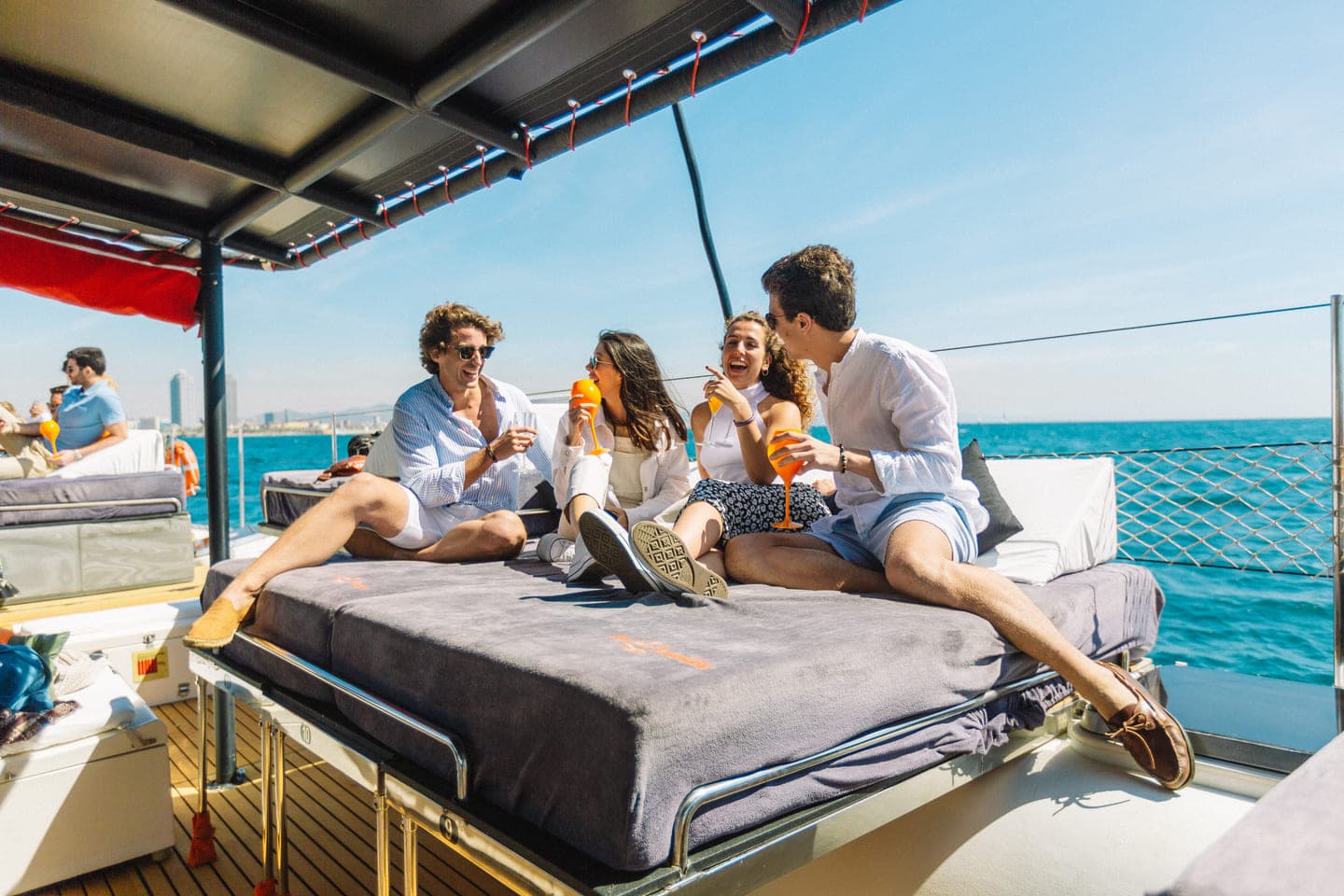 Grupo de amigos brindando con cócteles Aperol en la proa de un catamarán con la costa de Barcelona al fondo