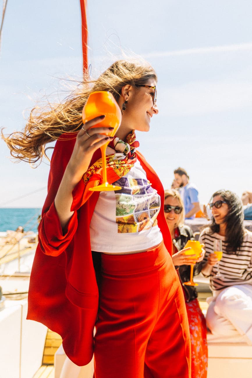 Mujer con conjunto rojo y cóctel naranja disfrutando del viento en cubierta
