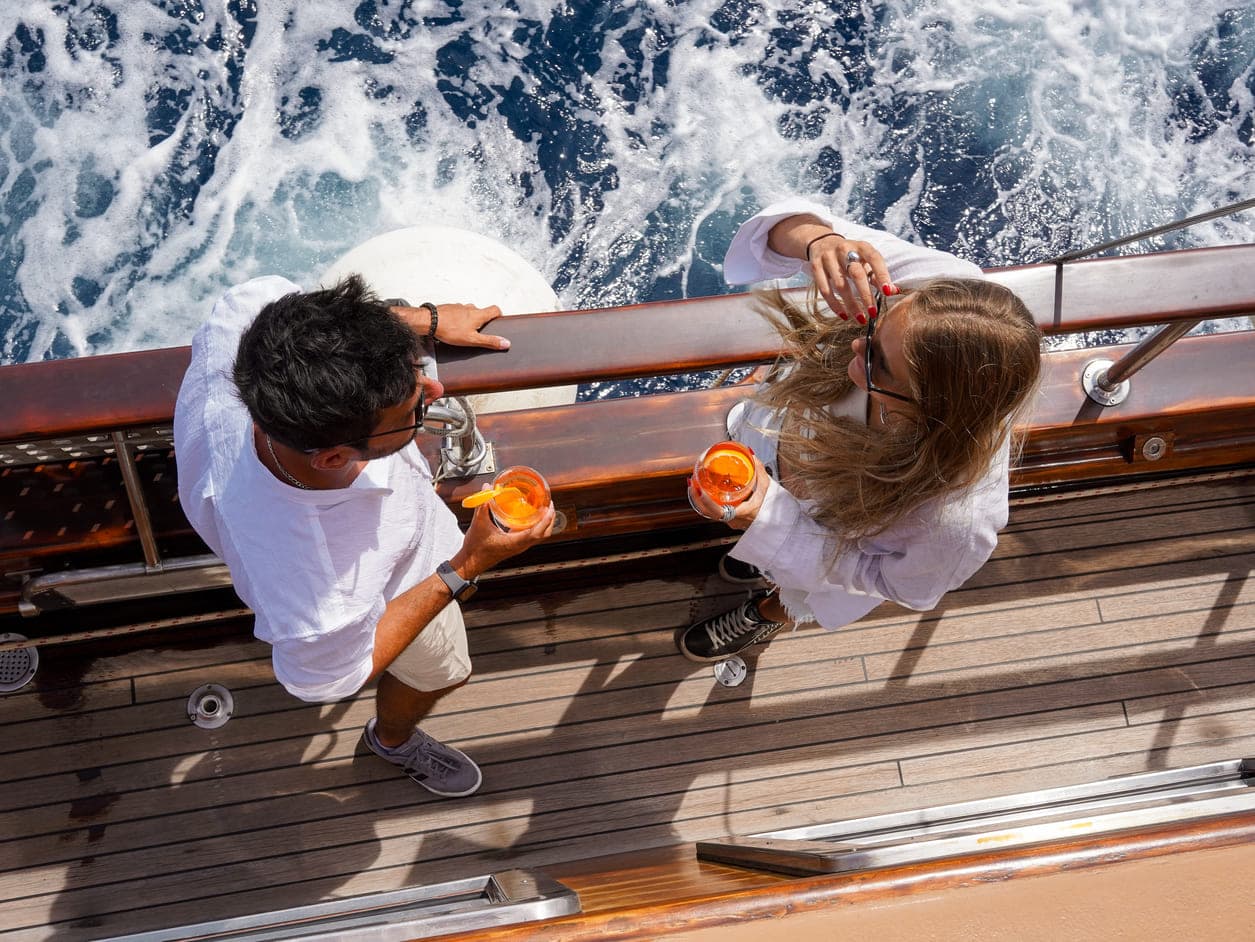 Vista aérea de dos personas bebiendo Aperol spritz en la cubierta de madera de un velero