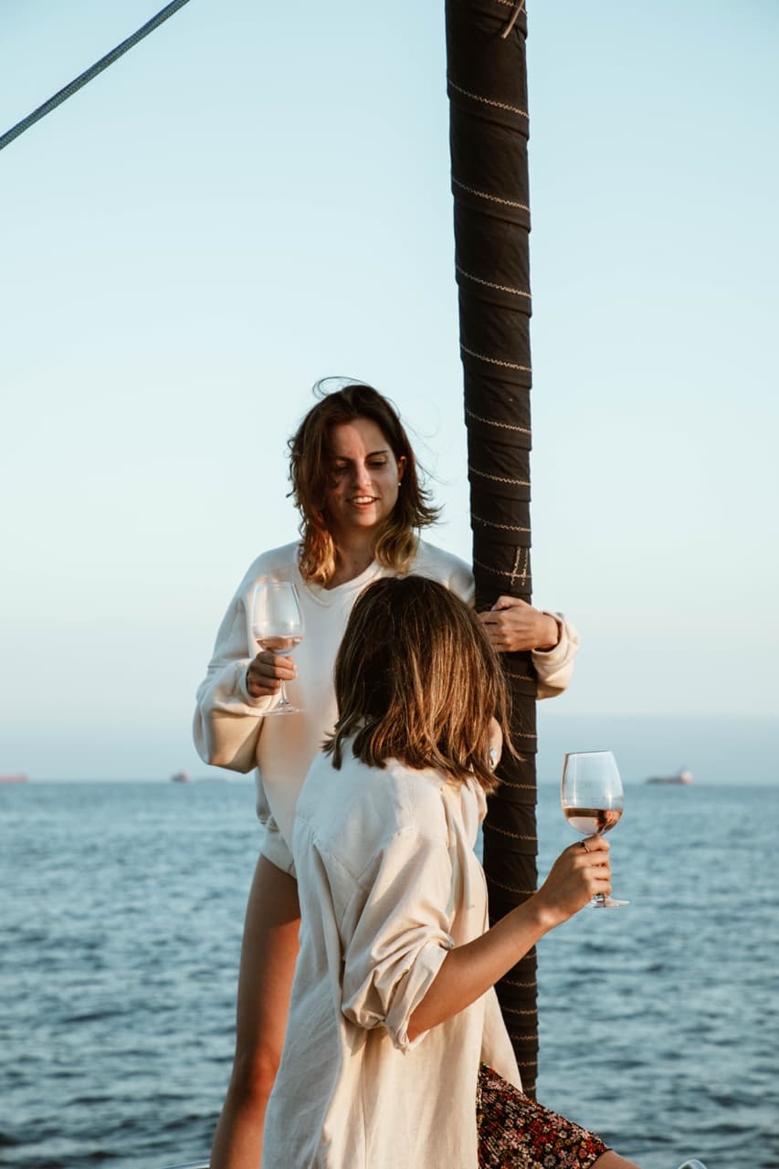 Dos amigas brindando con copas de vino en la cubierta de un velero al atardecer