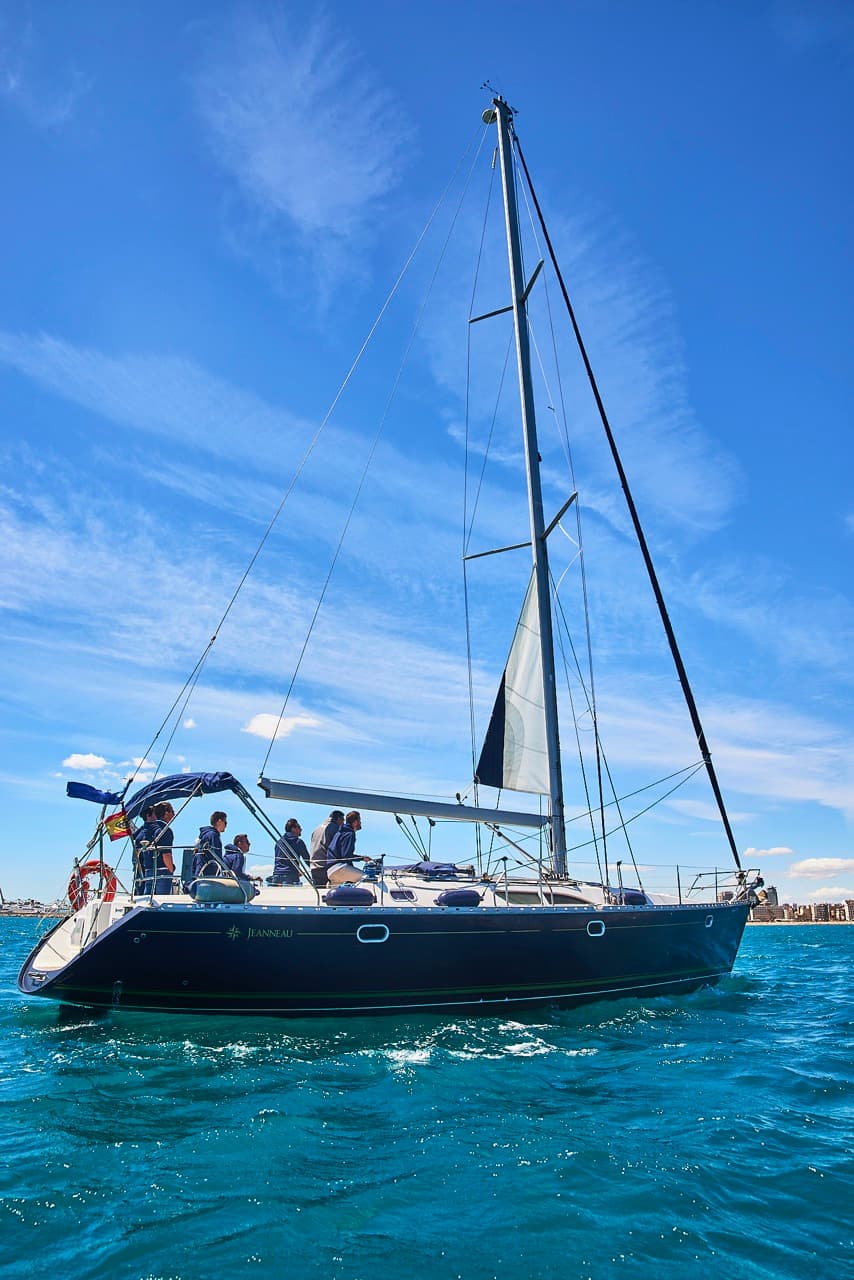 Velero de casco azul marino navegando con la tripulación a bordo bajo un cielo despejado