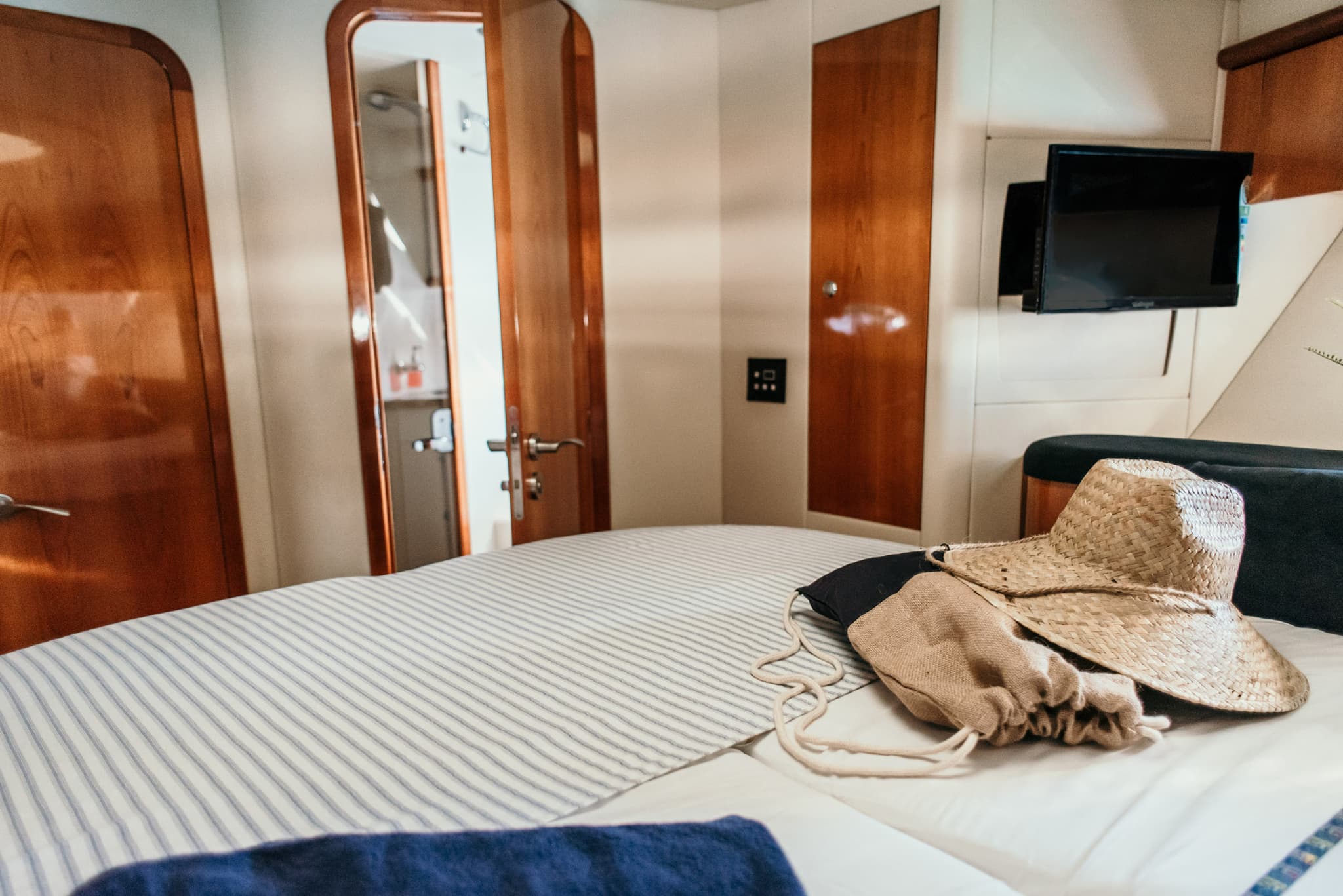 Camarote del yate con baño privado, televisor y bolsa de playa con sombrero sobre la cama