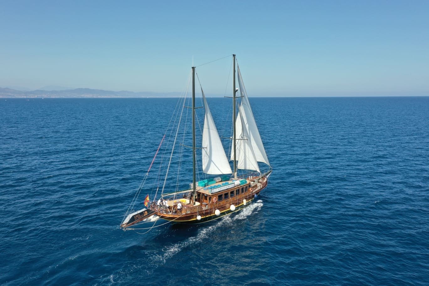 Vista aérea de un velero de dos palos con las velas blancas desplegadas navegando en el mar