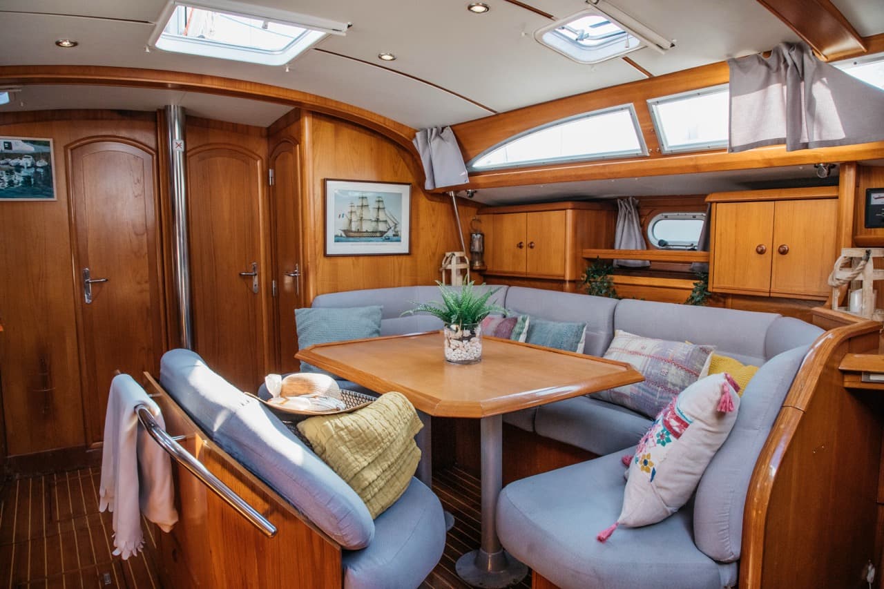 Salón interior de un velero con asientos tapizados en azul y mesa de comedor de madera