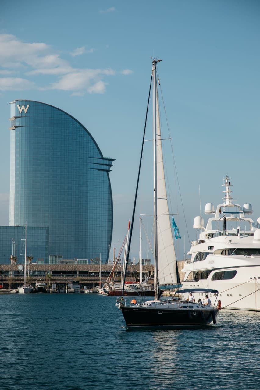 Velero navegando en el puerto de Barcelona con el hotel W y un yate de lujo al fondo