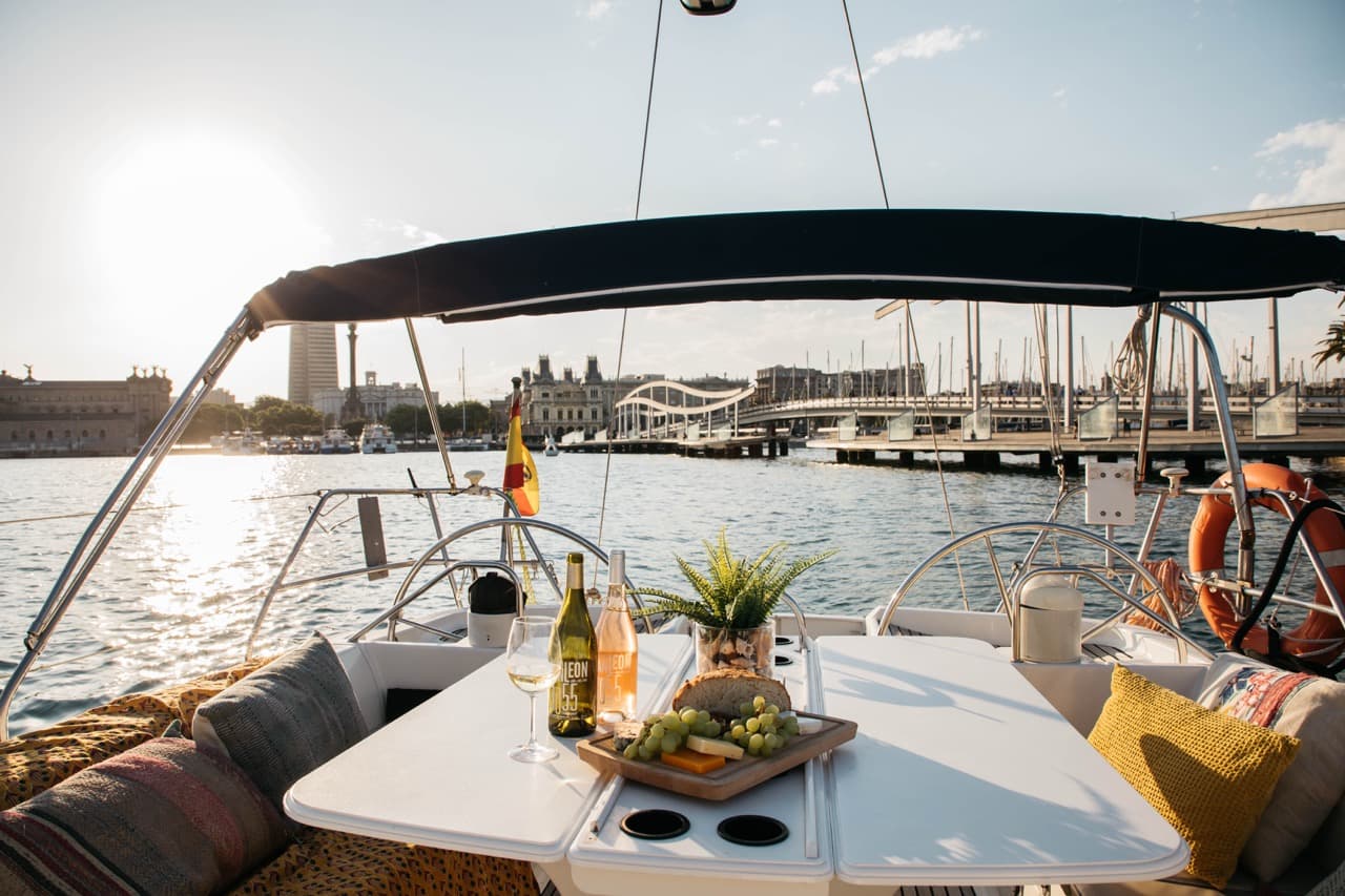 Mesa con vino, quesos y uvas en la cubierta de un velero al atardecer con vistas al puerto