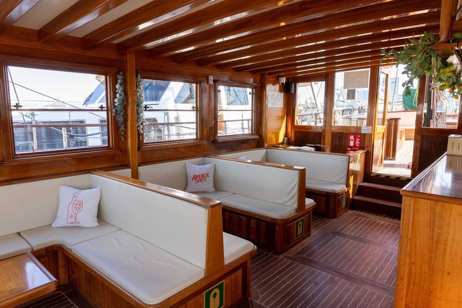 Salón interior de madera de un velero con bancos blancos y cojines junto a las ventanas