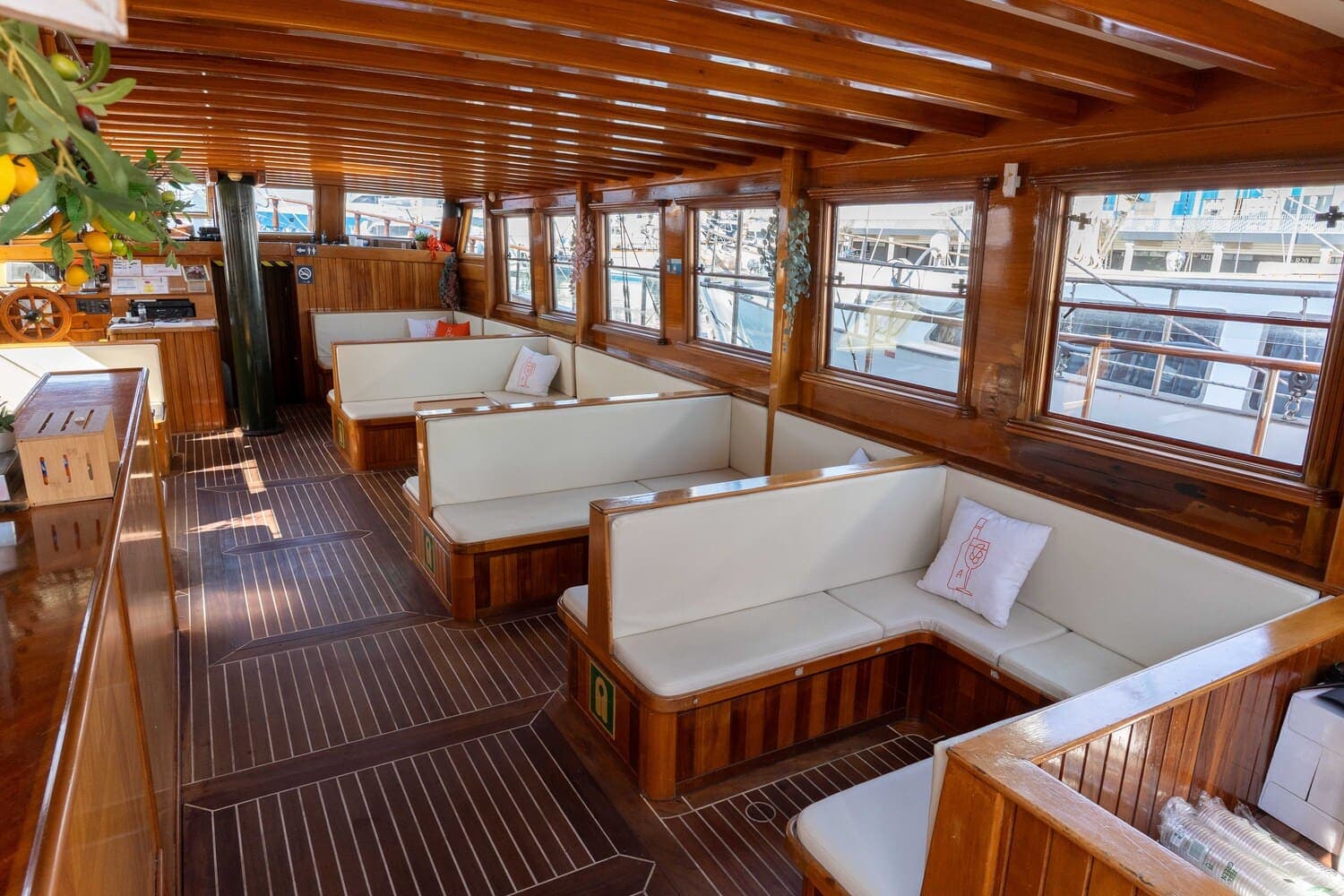 Salón interior de madera de un velero con bancos blancos en forma de U junto a las ventanas