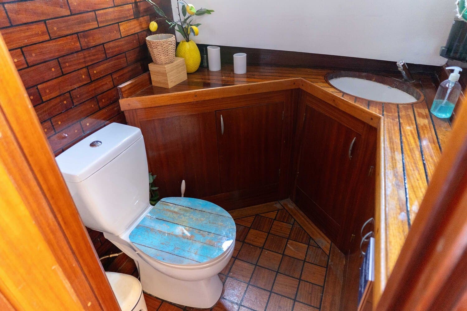 Aseo de madera a bordo de un velero con inodoro de tapa azul envejecida y planta decorativa
