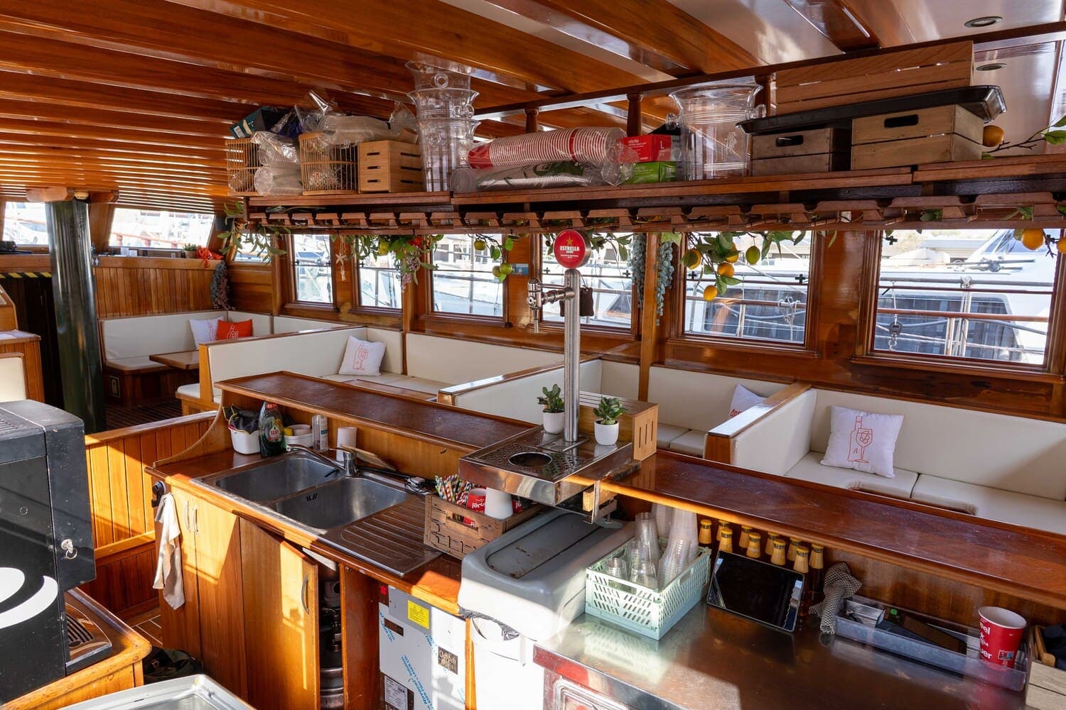 Barra con grifo de cerveza en el salón de madera de un velero decorado con cítricos colgantes