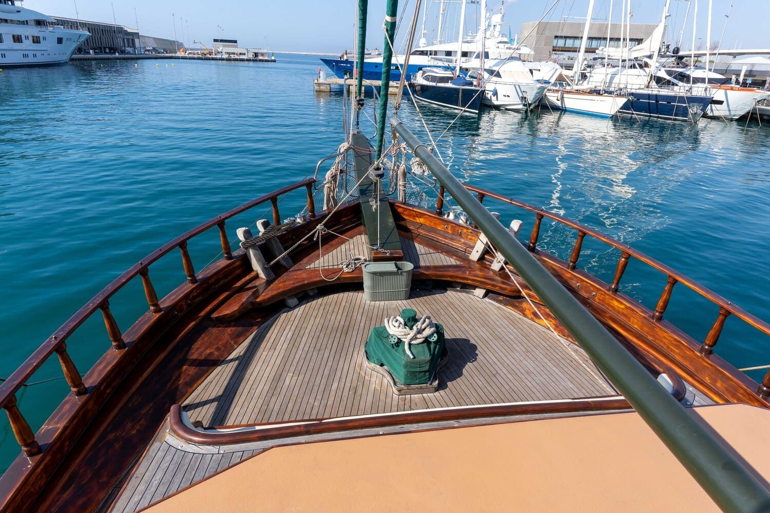 Proa de madera de un velero amarrado en el puerto con otros yates al fondo