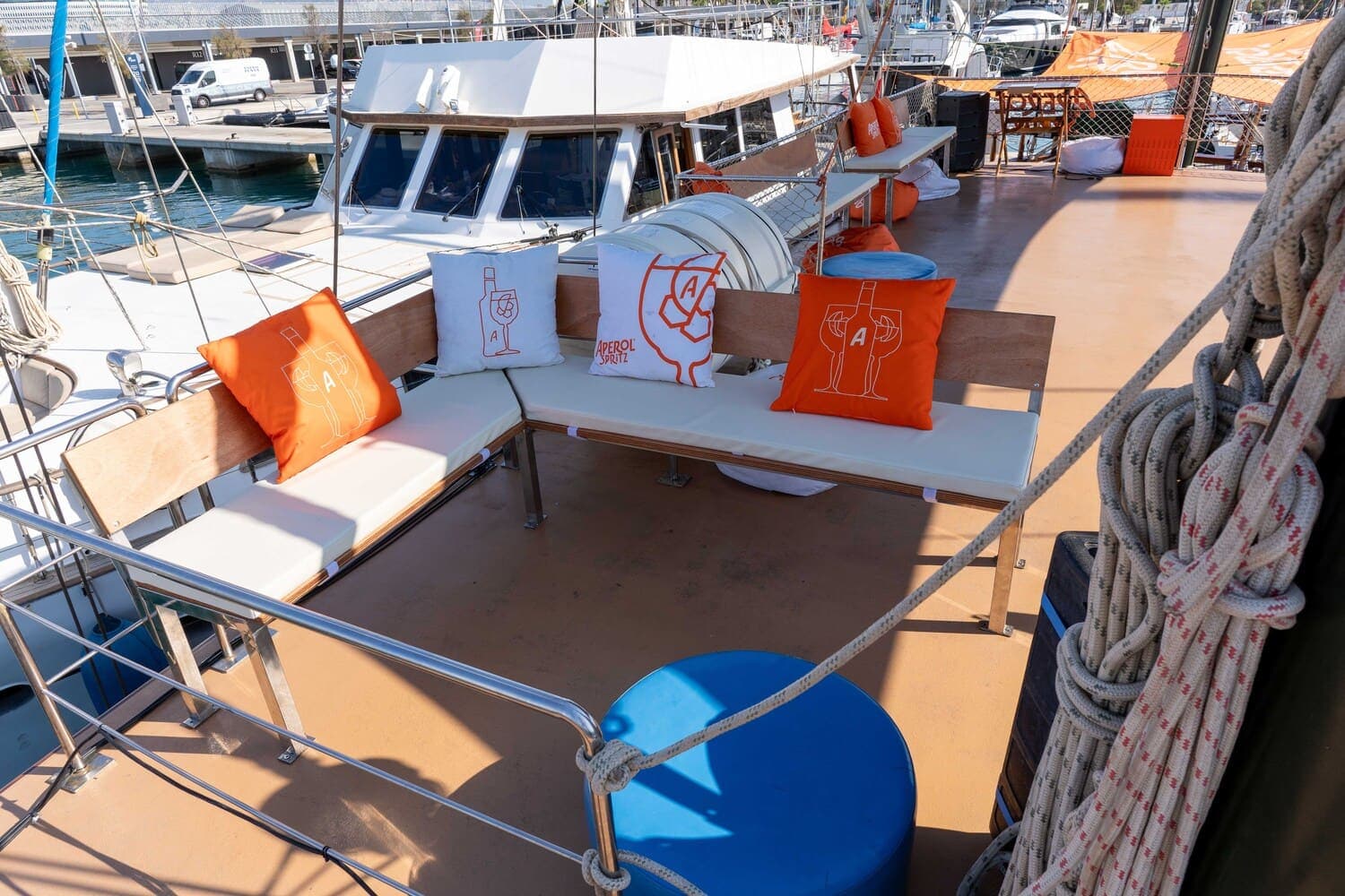 Zona de estar en cubierta de goleta con cojines Aperol Spritz, amarrada en el puerto