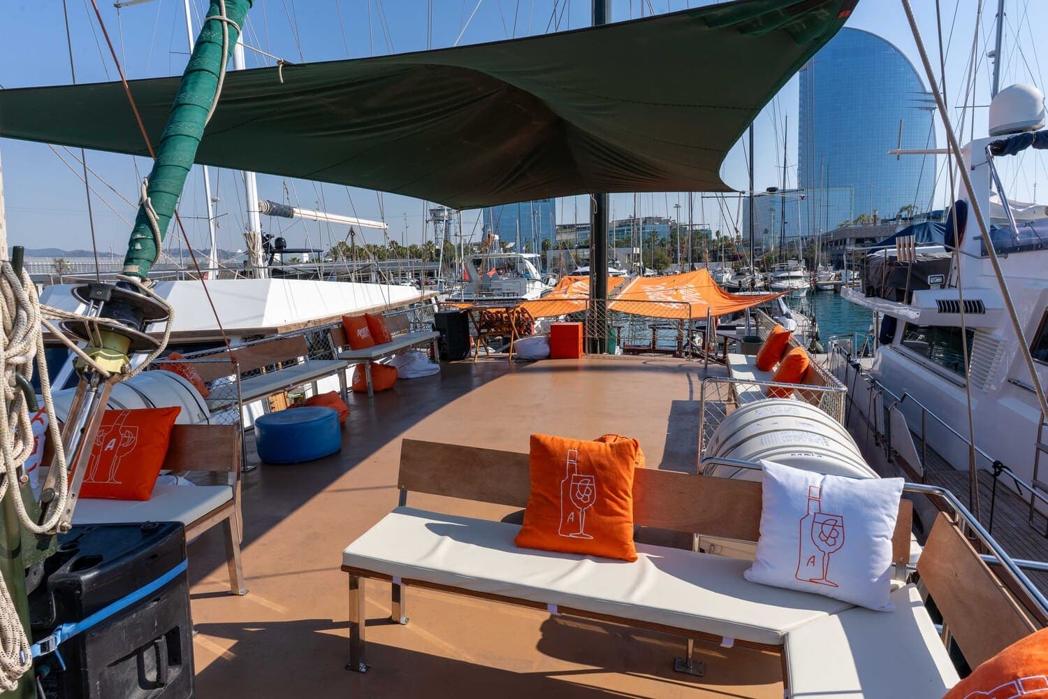 Cubierta de goleta con toldo y cojines Aperol Spritz, con el Hotel W de Barcelona al fondo