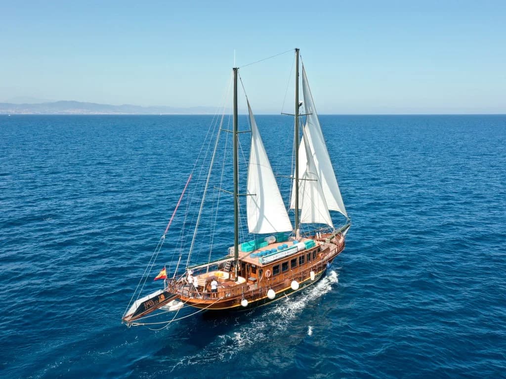 Vista aérea de una goleta de madera de dos palos navegando a vela sobre un mar azul intenso