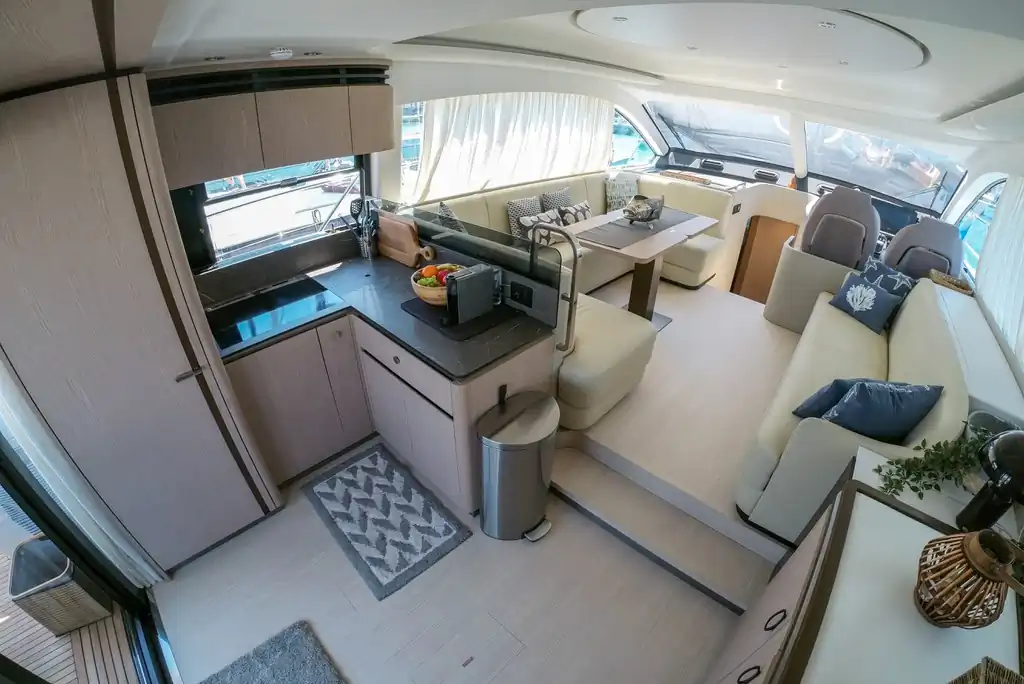 Salón interior de yate con cocina, sofás color crema y zona de comedor con grandes ventanales