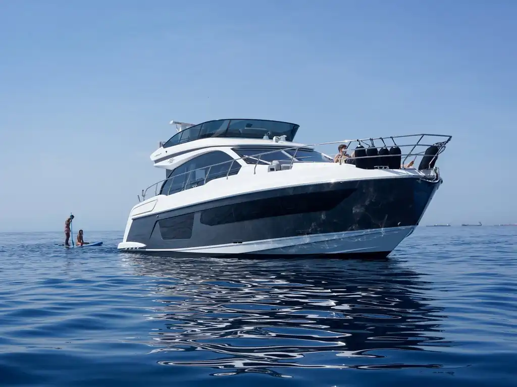Yate a motor Azimut fondeado en aguas azules con dos personas haciendo paddle surf al lado