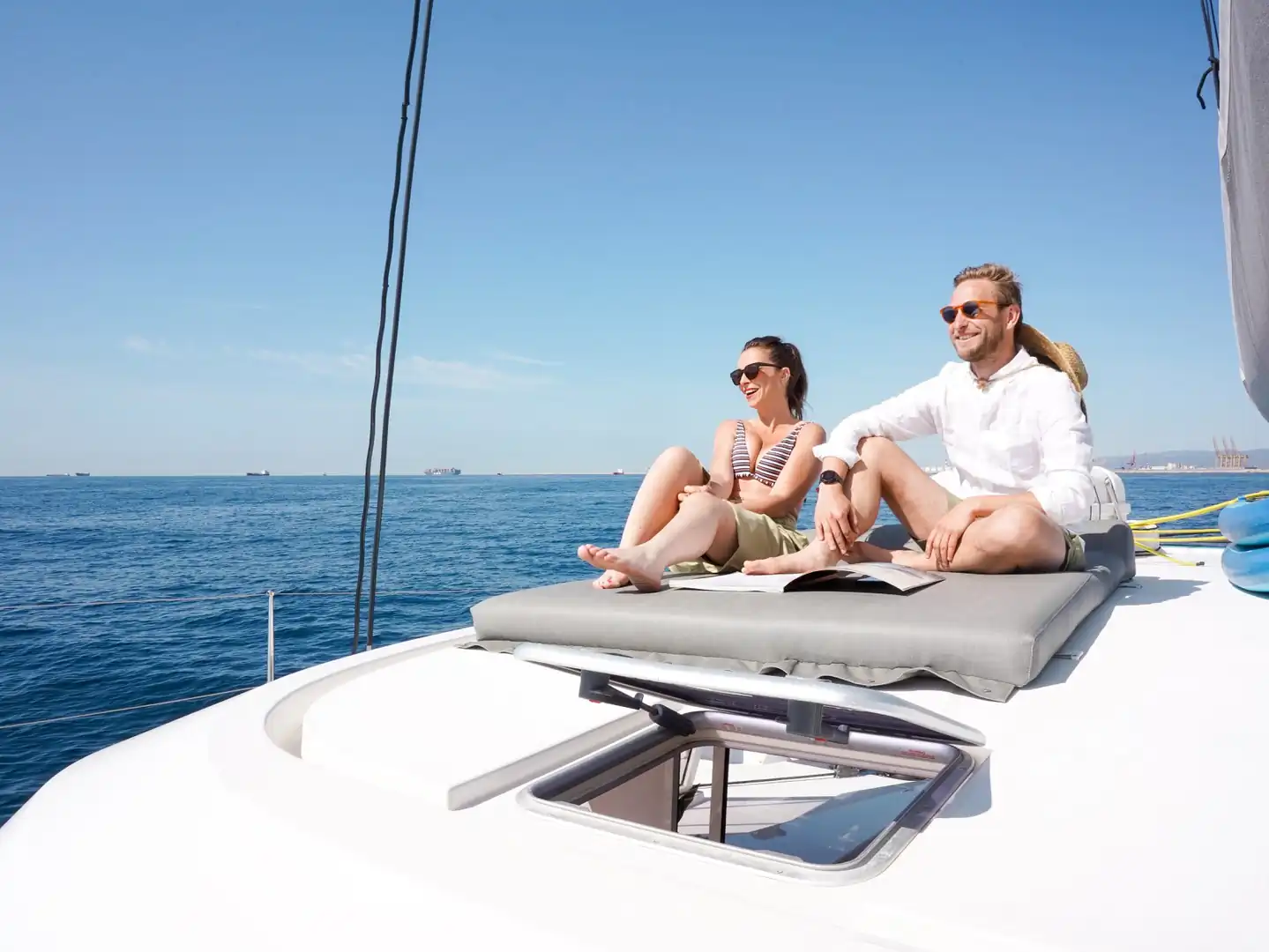 Pareja tomando el sol sobre el cojín de proa de un catamarán en aguas azules