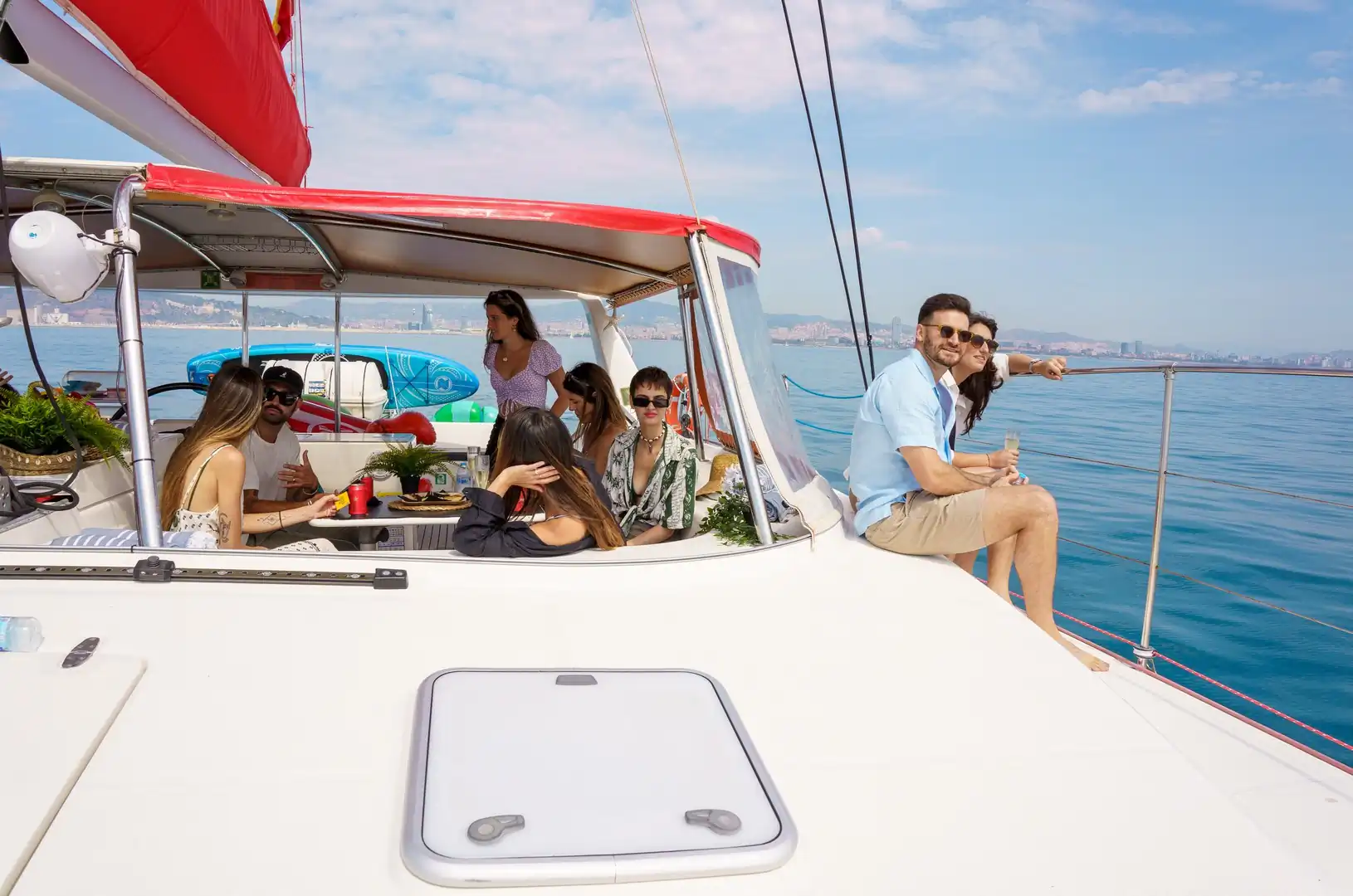 Grupo de amigos disfrutando en la bañera de un catamarán con el skyline de Barcelona al fondo