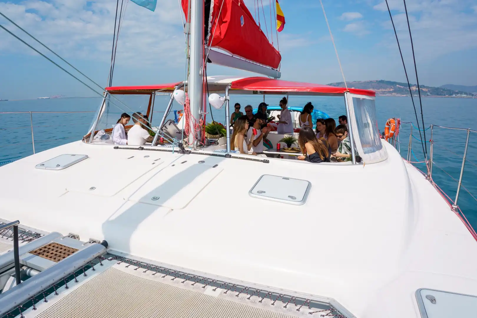 Vista de proa de un catamarán con pasajeros reunidos bajo el toldo rojo de la bañera