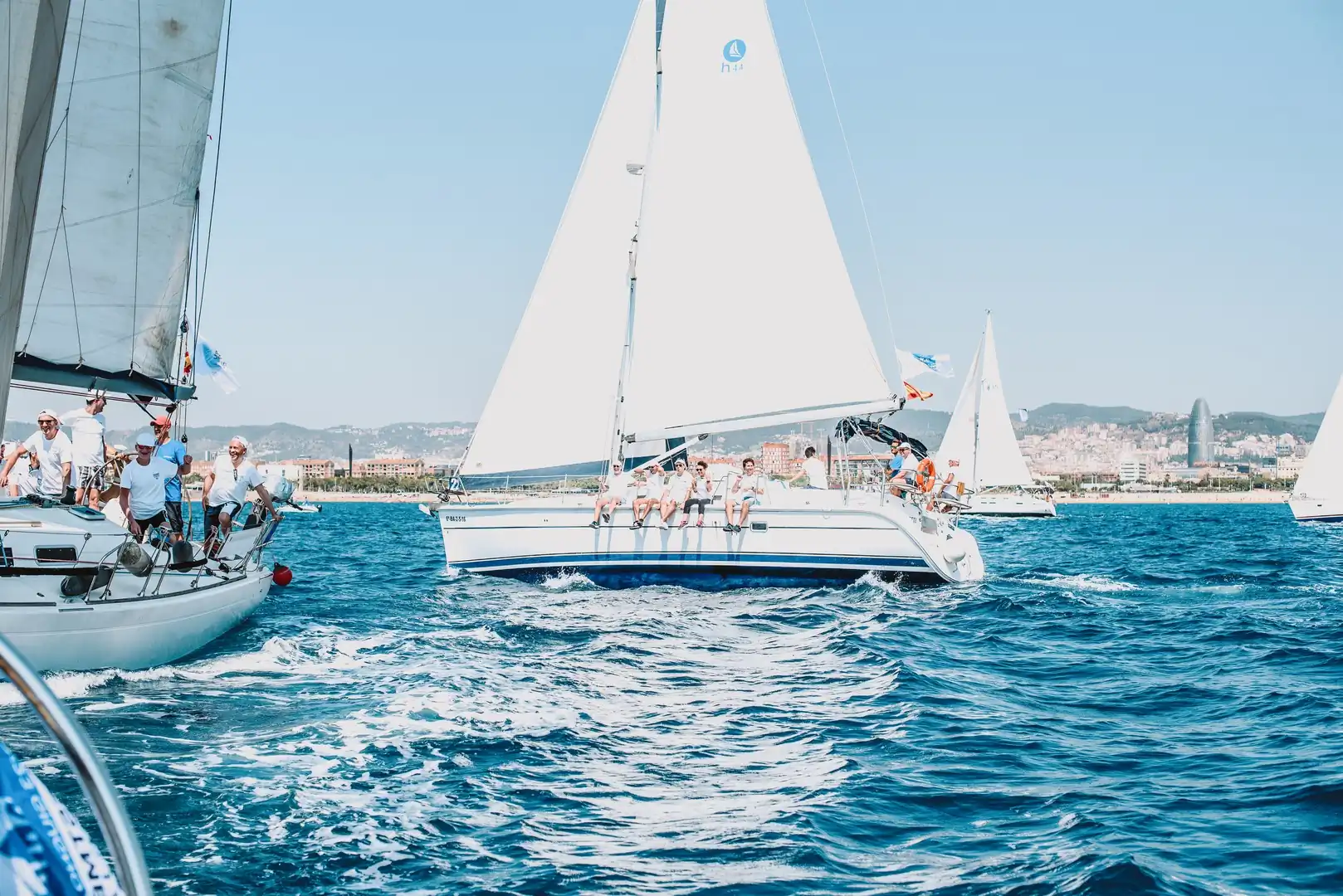 Velero con la tripulación sentada en la borda navegando en regata frente al skyline de Barcelona