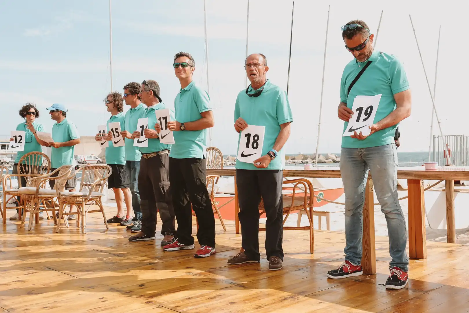Participantes con polo turquesa sostienen sus dorsales numerados antes de la regata en el puerto