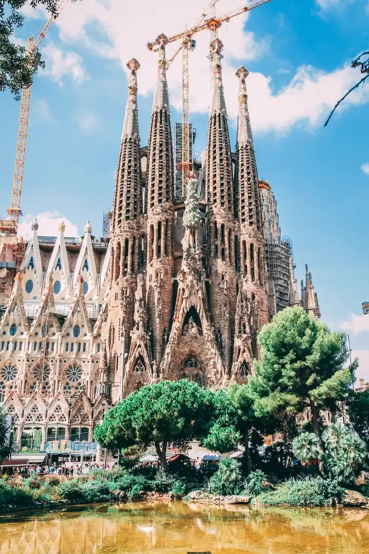 Fachada de la Sagrada Família con grúas de construcción y vegetación