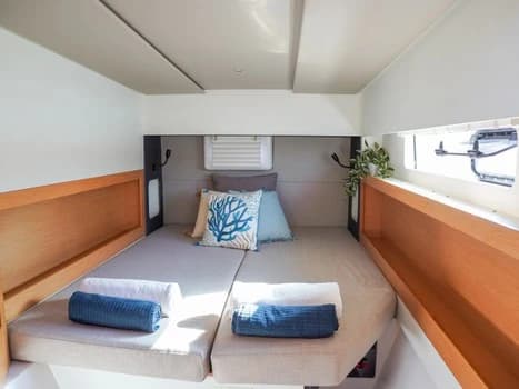 Camarote de catamarán con cama doble, maderas claras, cojín con motivo de coral y toallas azules
