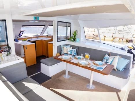 Salón de catamarán con mesa de comedor puesta y bancos tapizados junto a ventanales al mar