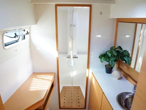 Baño de catamarán con ducha independiente acristalada, lavabo, planta y acabados en madera