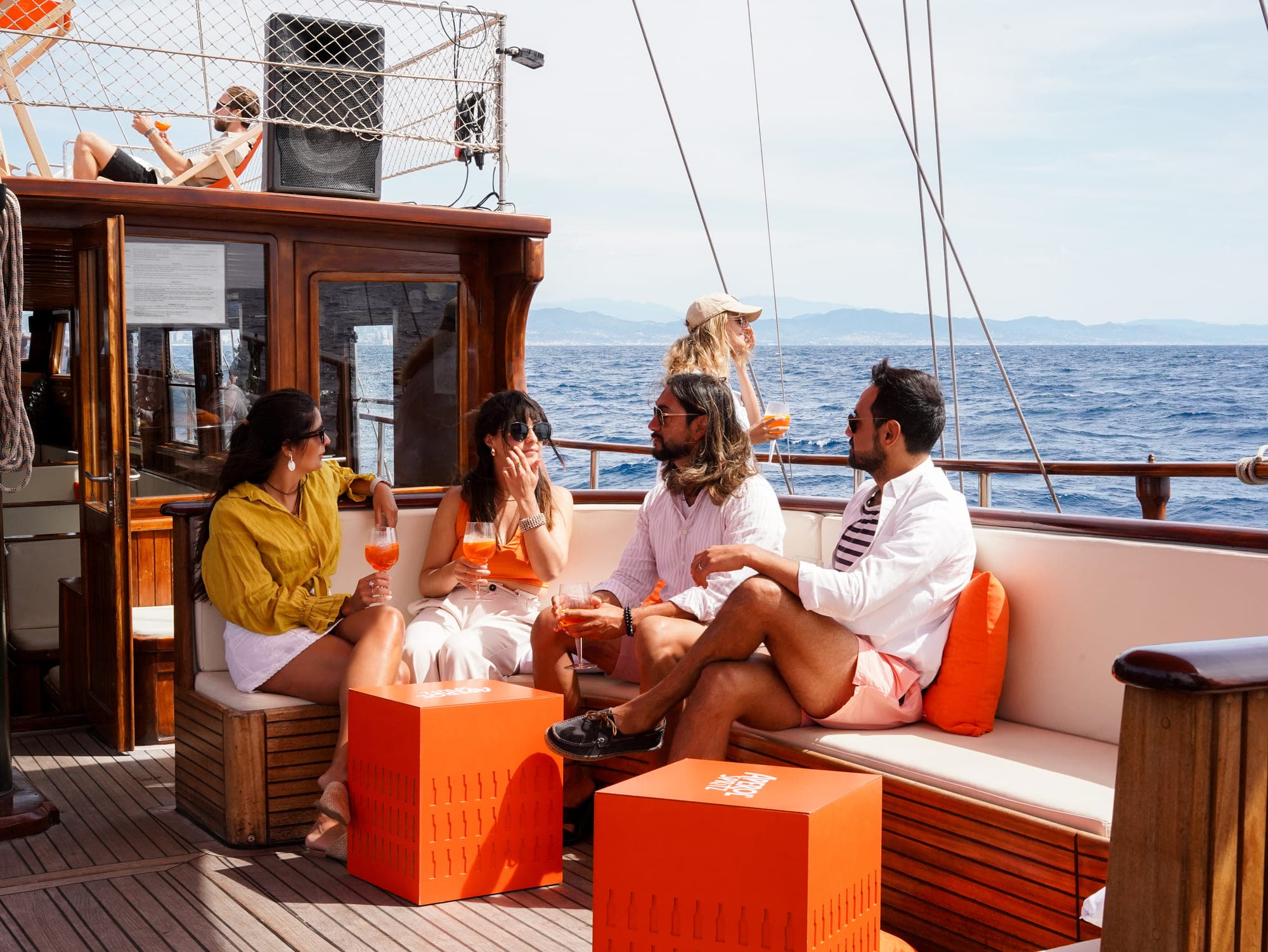 Grupo de amigos con cócteles Aperol Spritz relajados en la cubierta de la goleta navegando