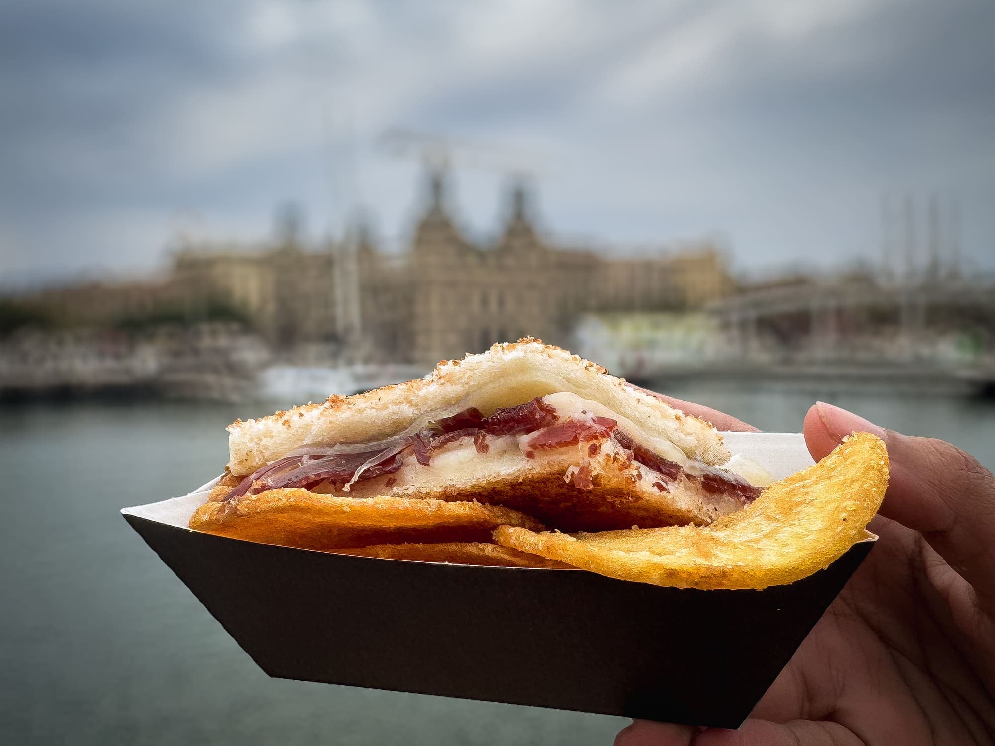 Primer plano del bocadillo de jamón sujeto en mano frente al puerto