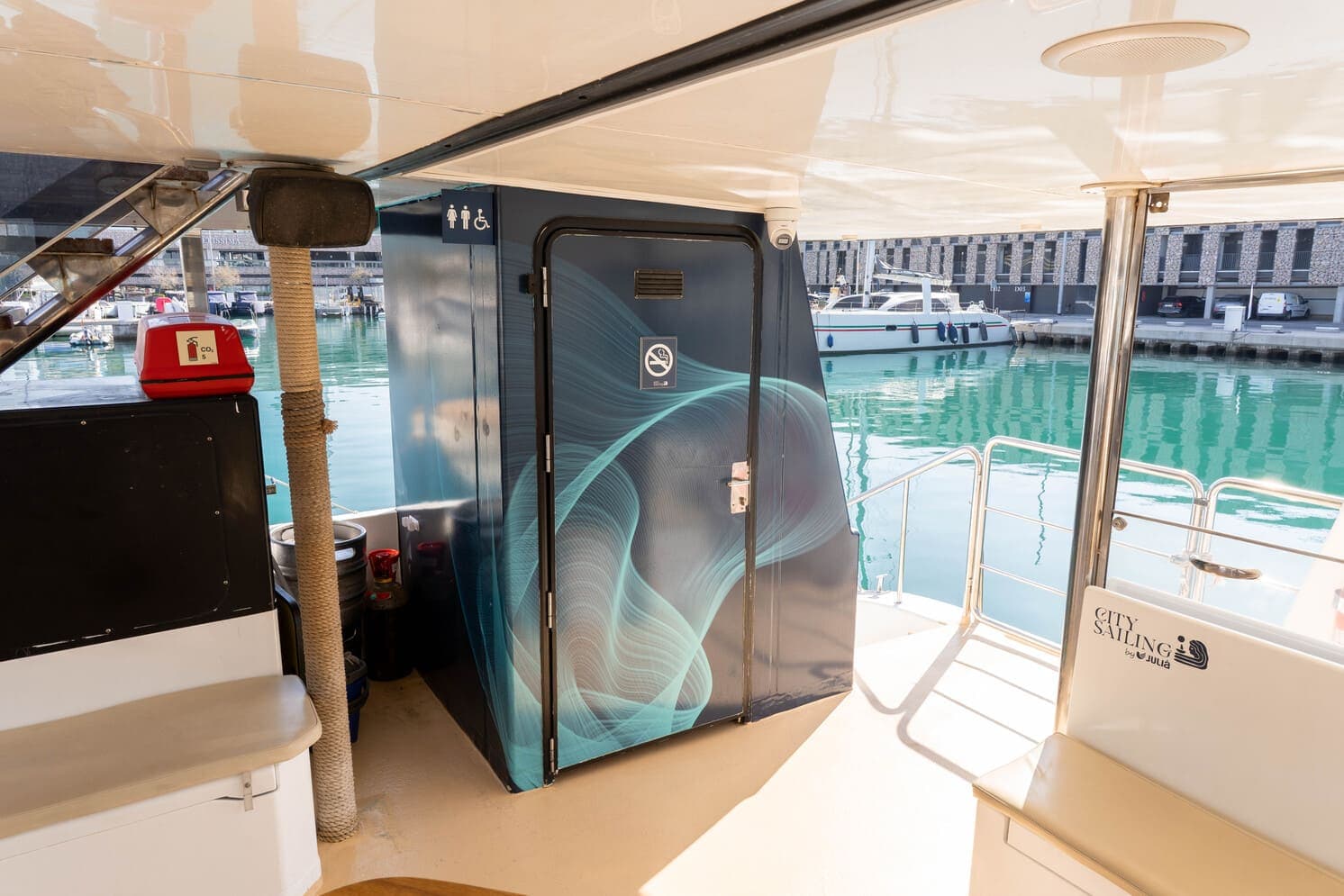 Puerta de aseo con diseño artístico en tonos azules a bordo de un catamarán amarrado