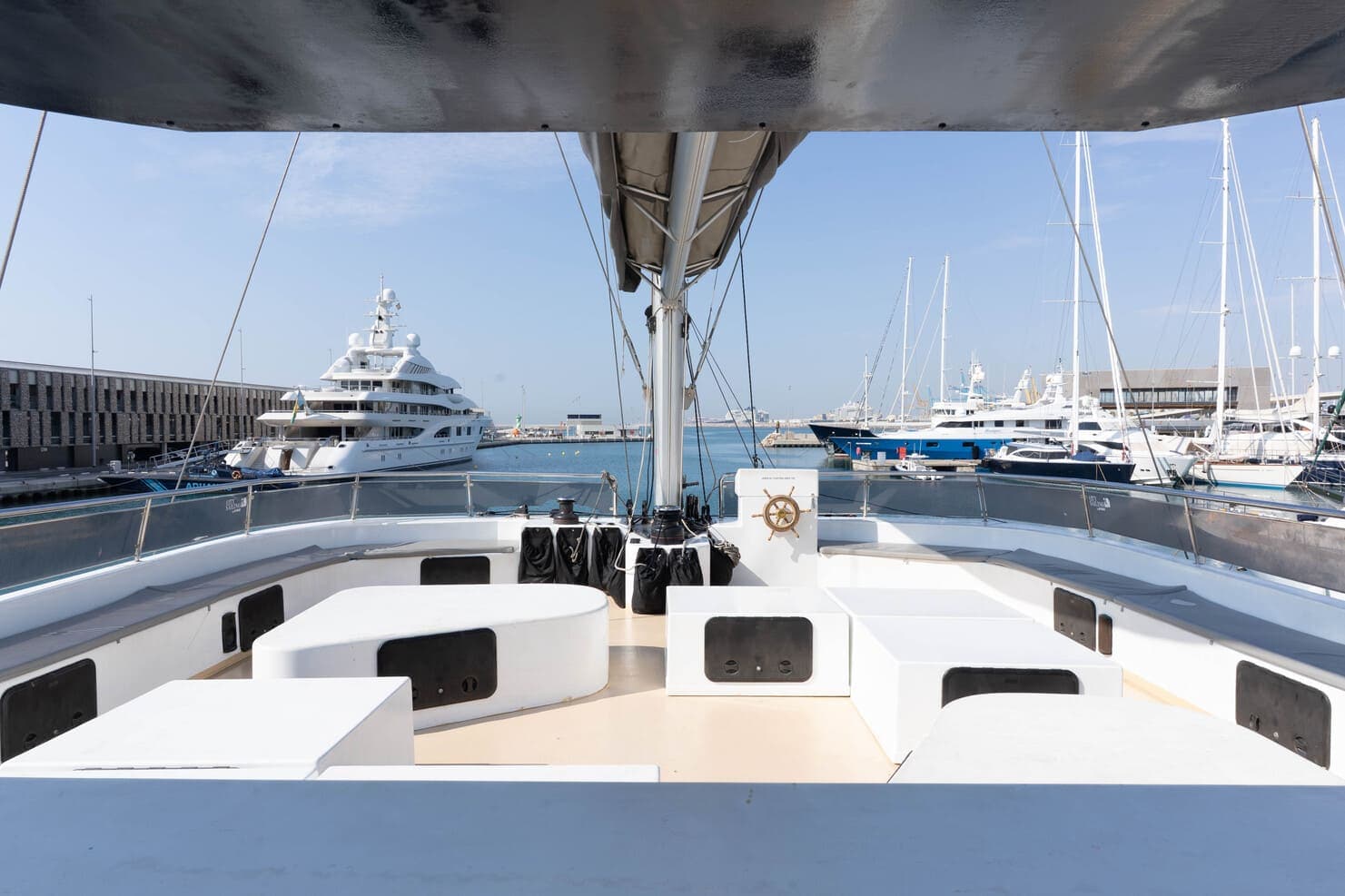 Cubierta de proa con asientos blancos de un catamarán, con un superyate amarrado al fondo