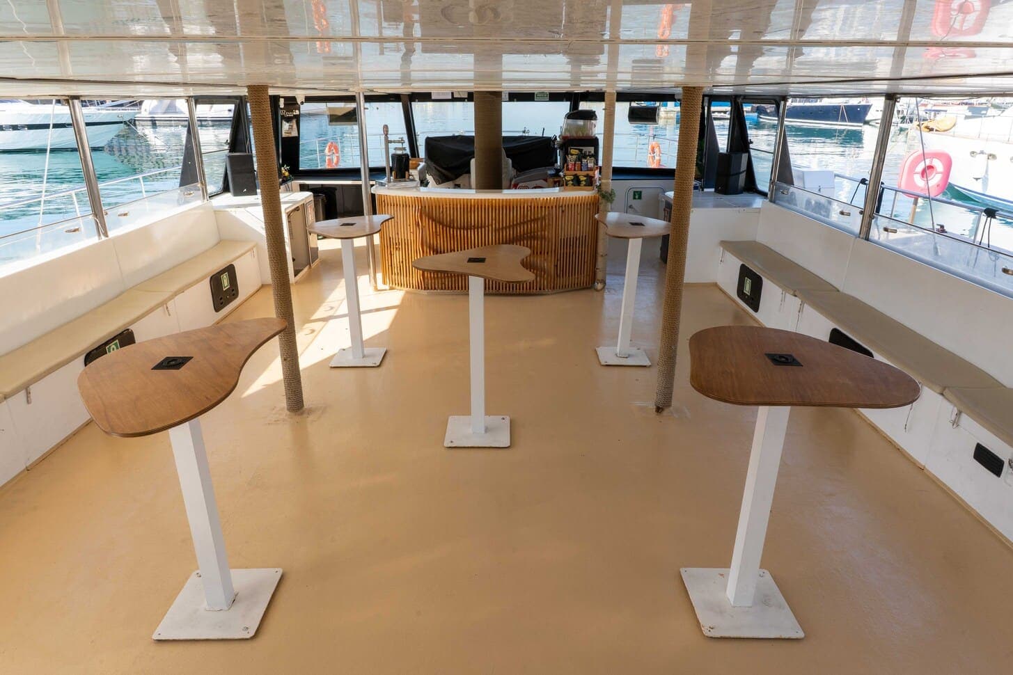 Zona de mesas altas y barra de madera en la cubierta interior de un catamarán amarrado en el puerto