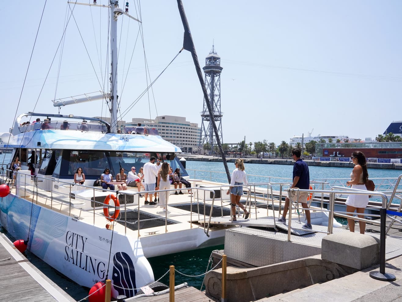 Catamarán amarrado en el muelle con pasajeros embarcando junto a la torre del teleférico de Barcelona