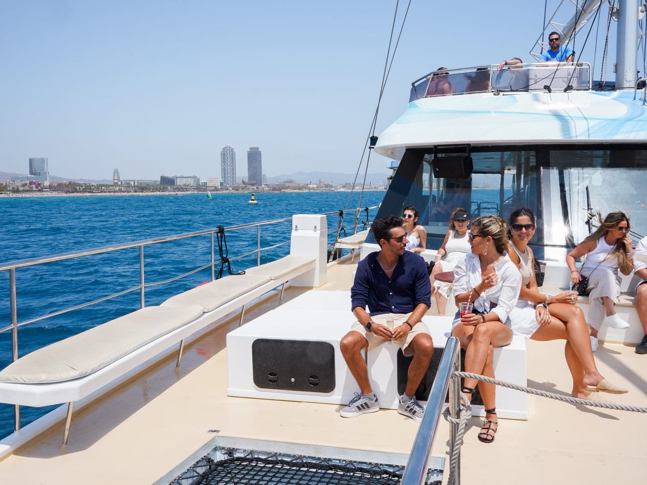 Grupo de amigos charlando y bebiendo en la cubierta de un catamarán con la playa de Barcelona al fondo