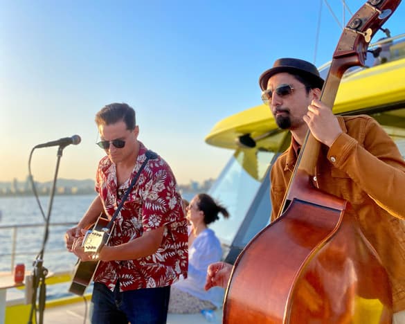 Músicos tocando guitarra y contrabajo a bordo del catamarán al atardecer