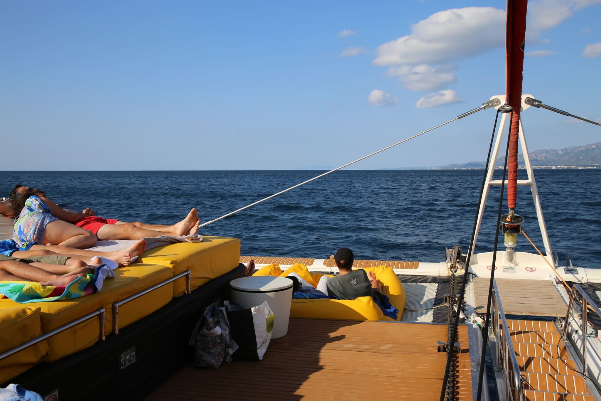 Pareja tumbada en los cojines amarillos de proa del catamarán con el mar de fondo