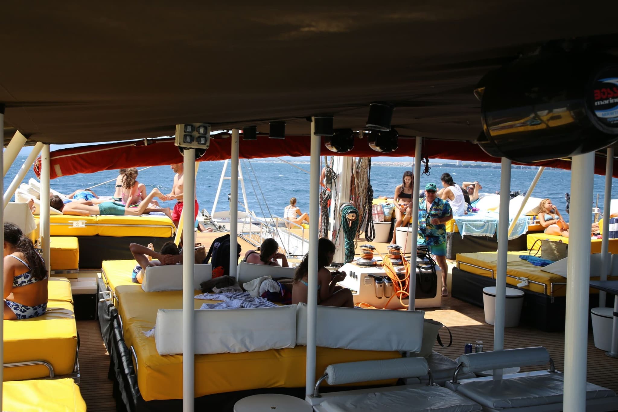 Pasajeros relajados bajo la lona del catamarán con el mar y la costa al fondo