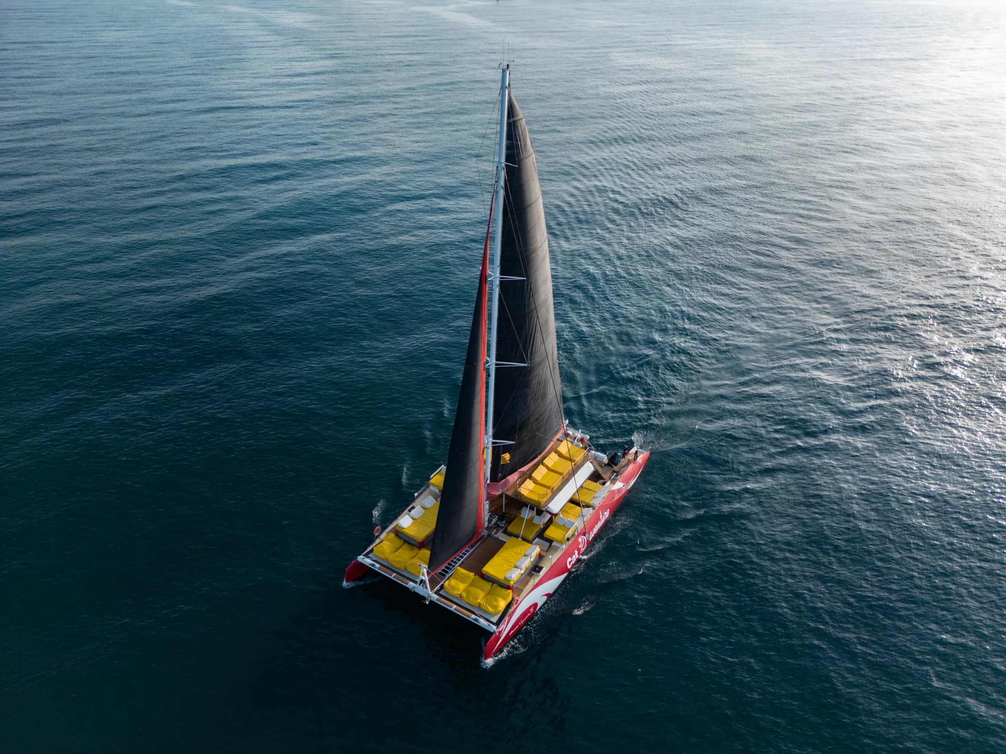 Vista aérea del catamarán navegando a toda vela sobre aguas azules y brillantes