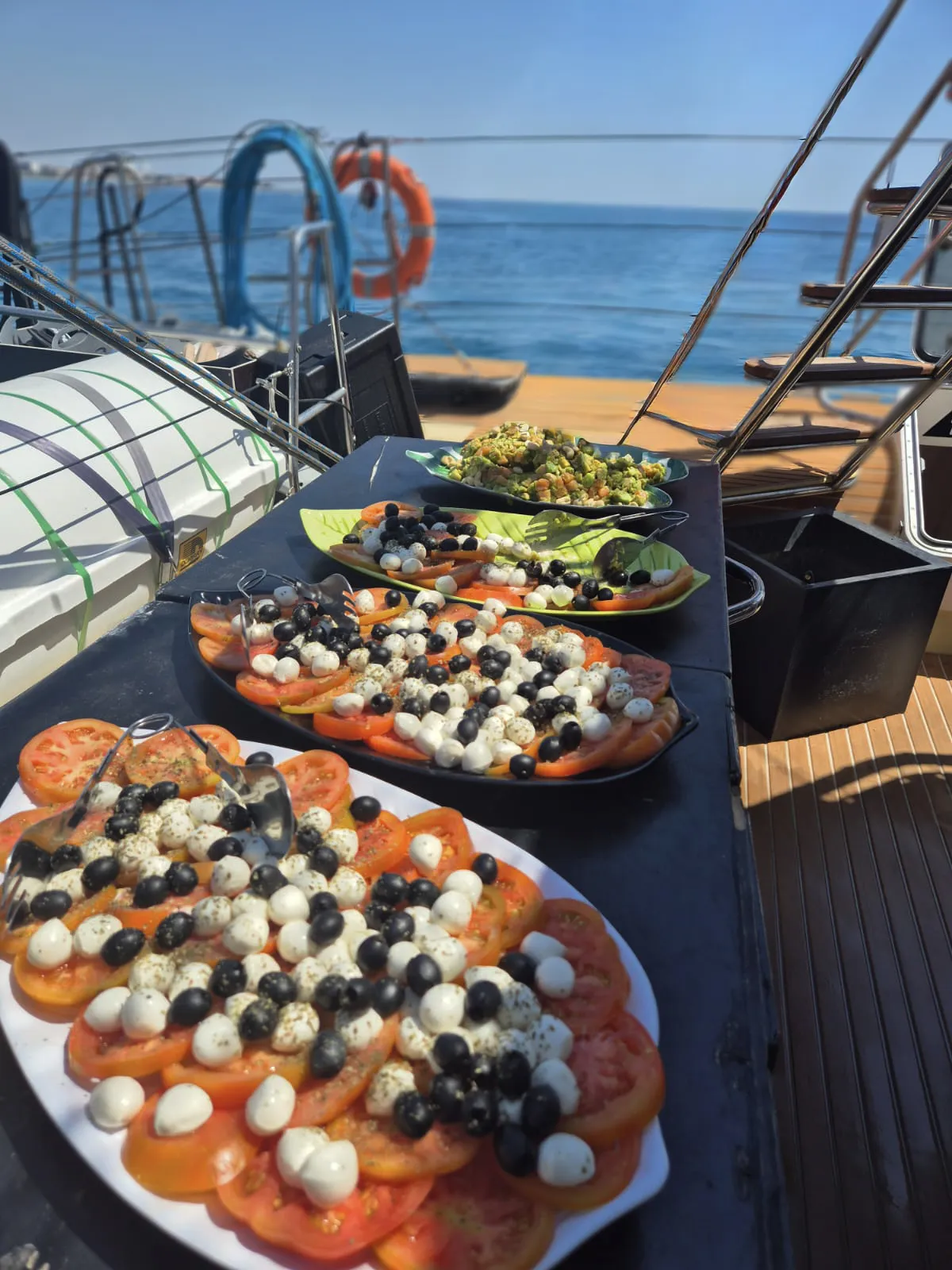 Bandejas de tomate con mozzarella y aceitunas dispuestas en la cubierta junto al mar