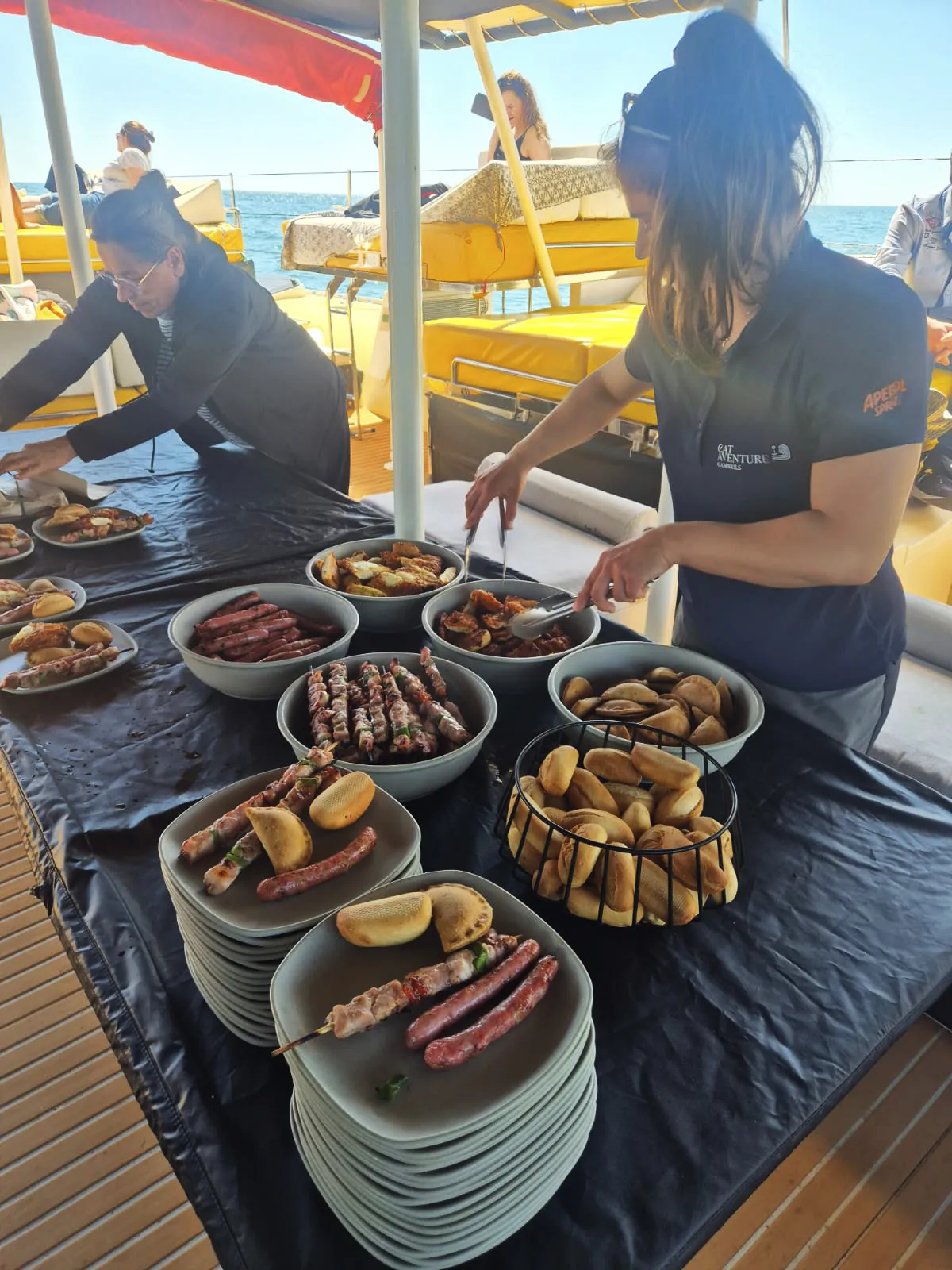 Tripulantes sirviendo brochetas, salchichas y pan recién asados en la barbacoa a bordo