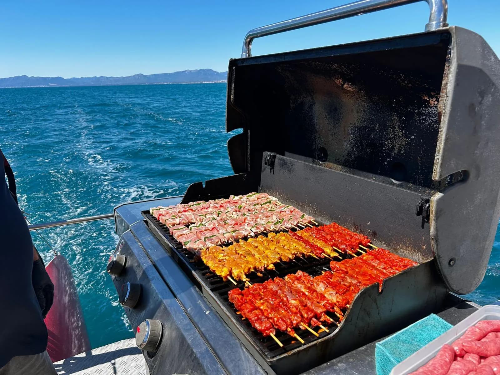 Brochetas de carne marinada asándose en la parrilla con el mar de fondo