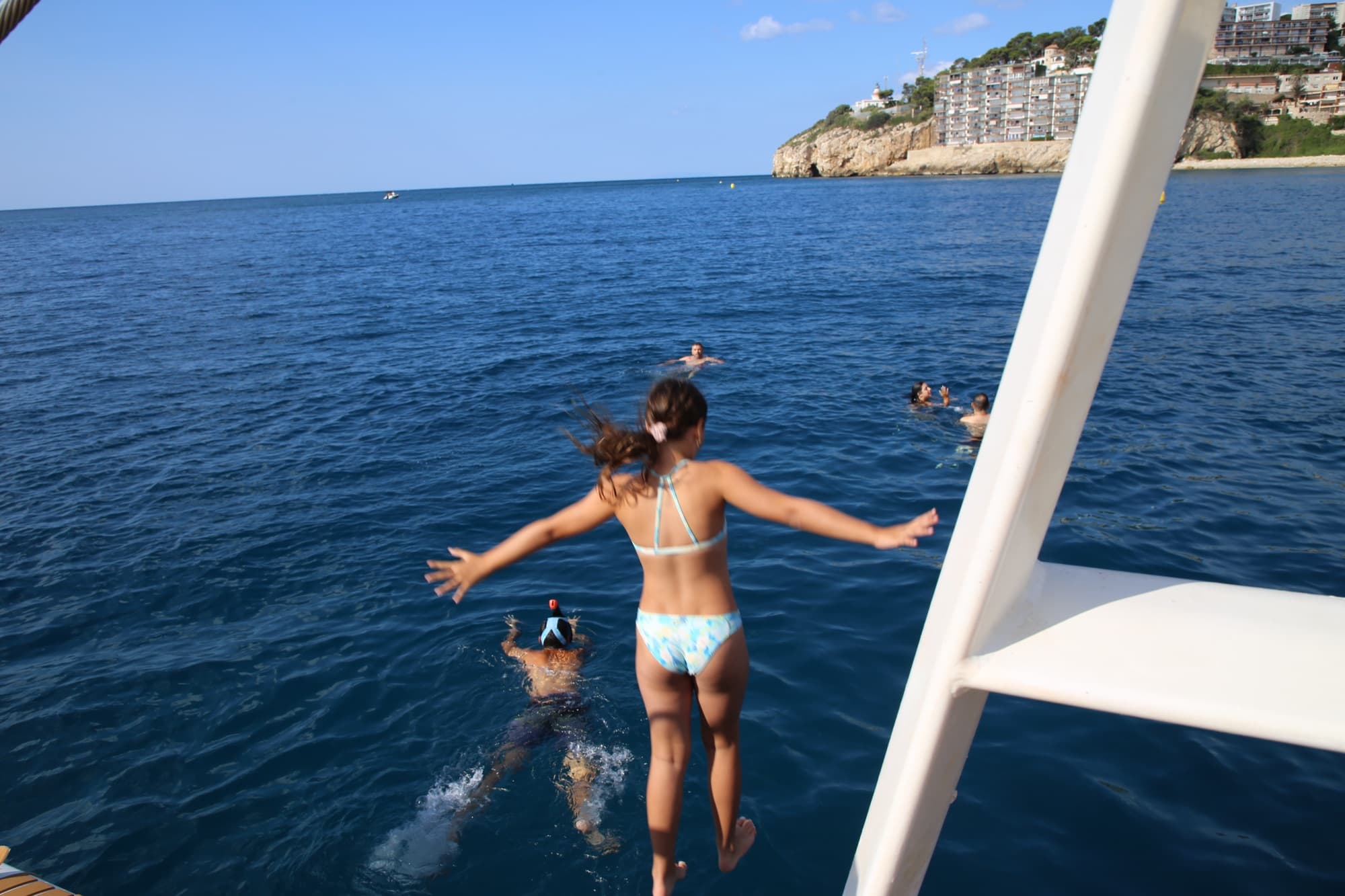 Niña saltando al mar desde la plataforma del catamarán frente a la costa de Cambrils