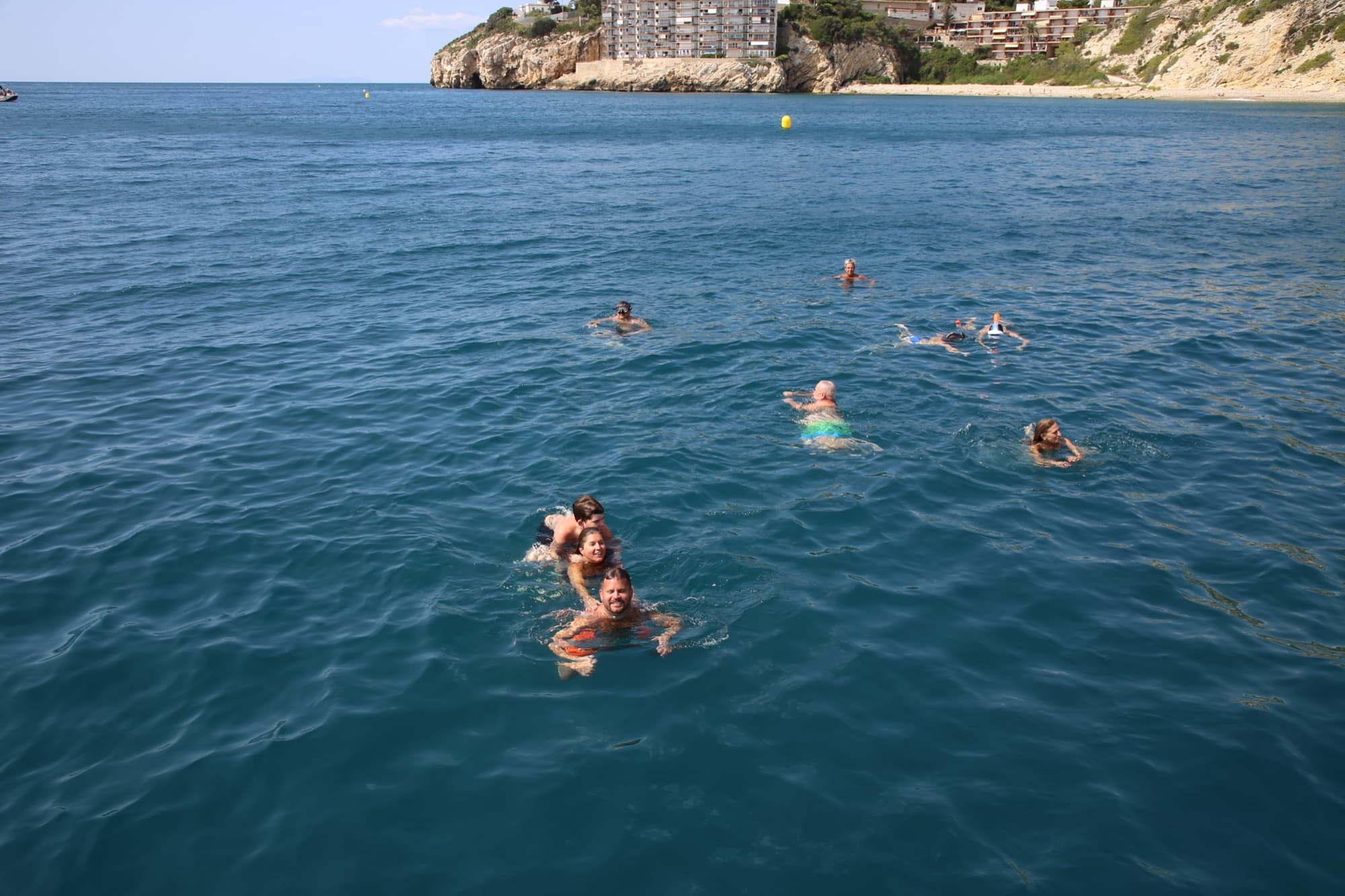 Grupo de bañistas nadando y sonriendo en el mar frente a la costa rocosa