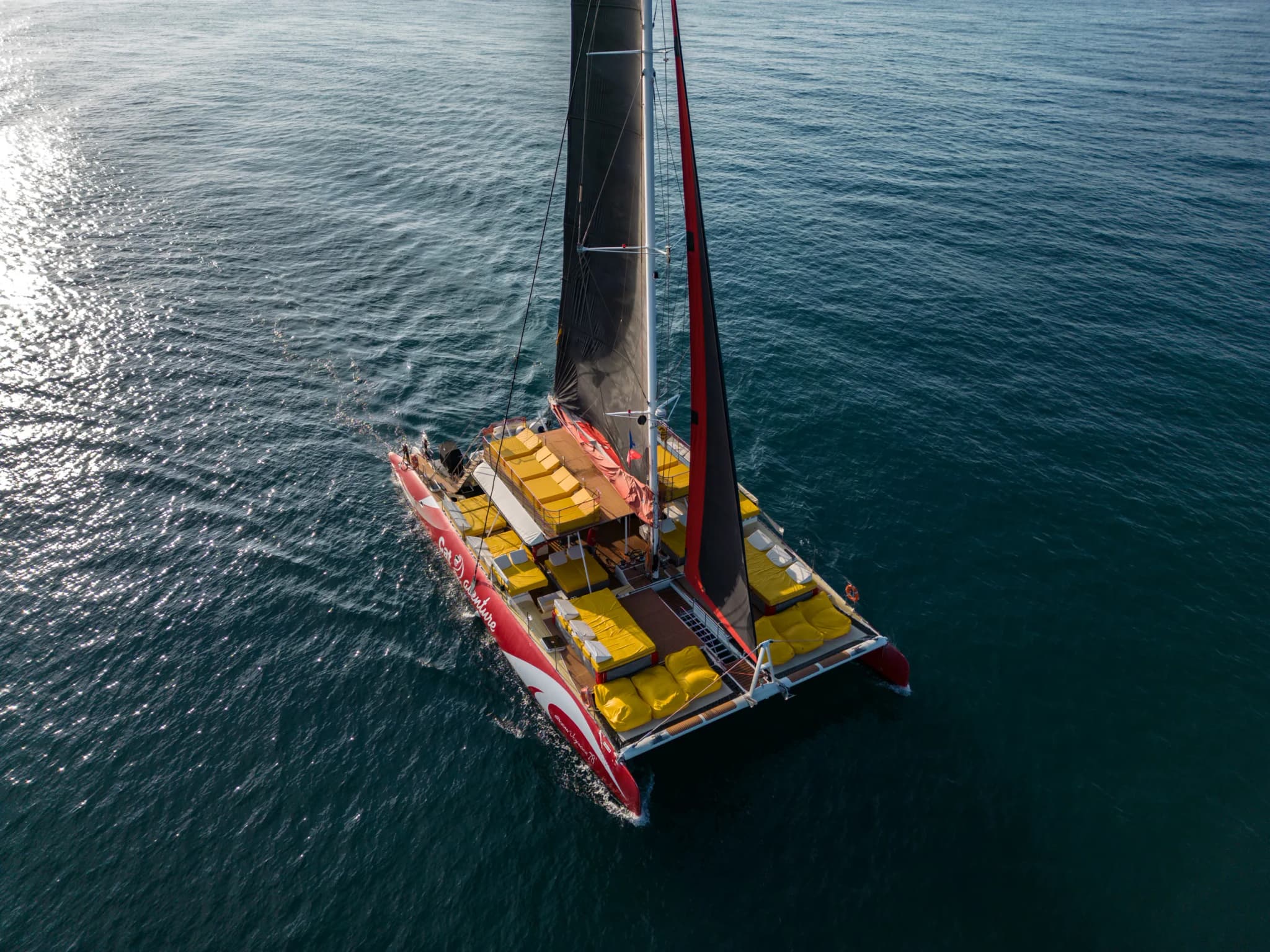 Catamarán con vela negra navegando en aguas tranquilas, visto desde el aire