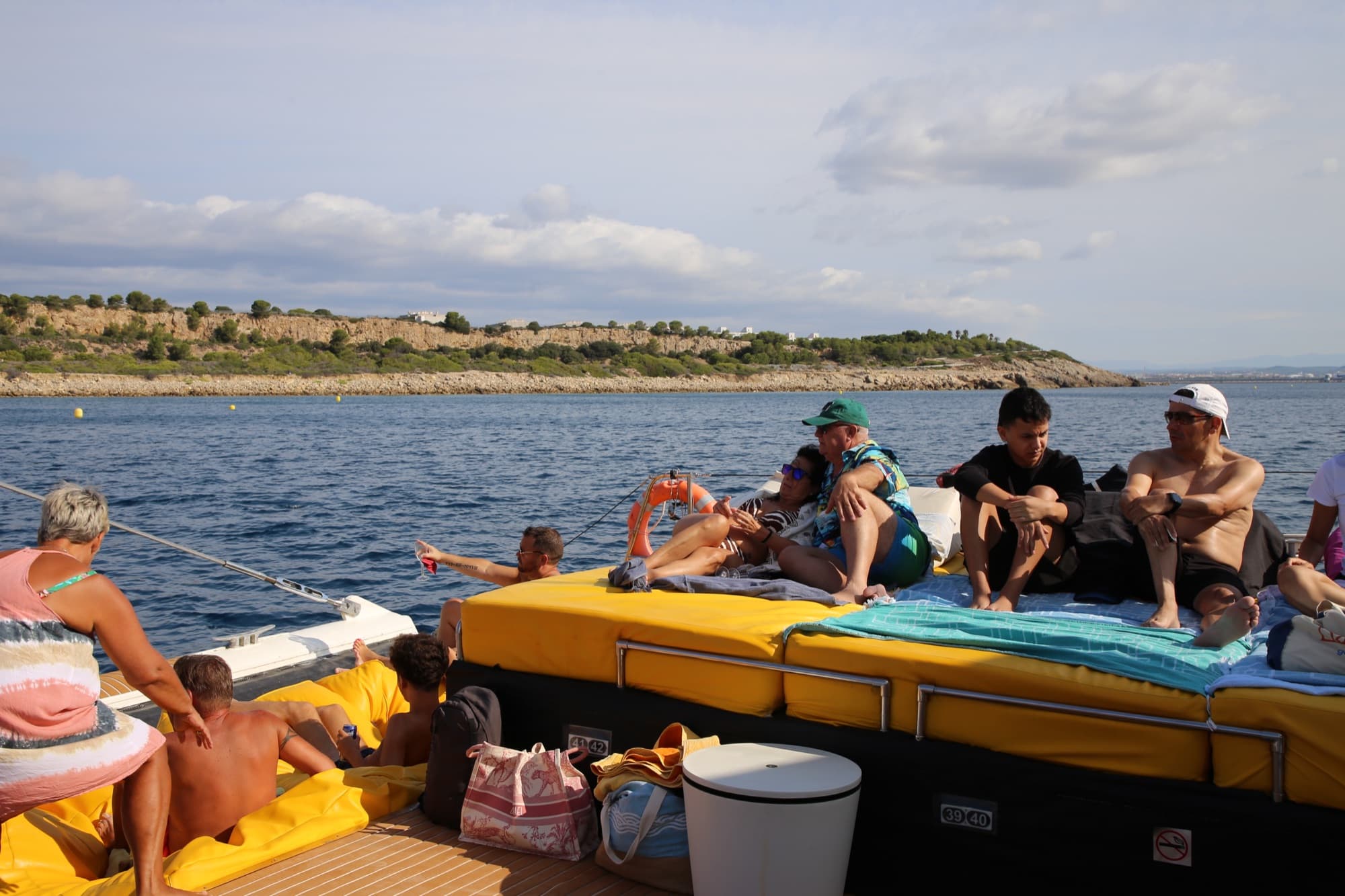 Grupo de amigos sentados juntos en la cama balinesa con la costa rocosa al fondo